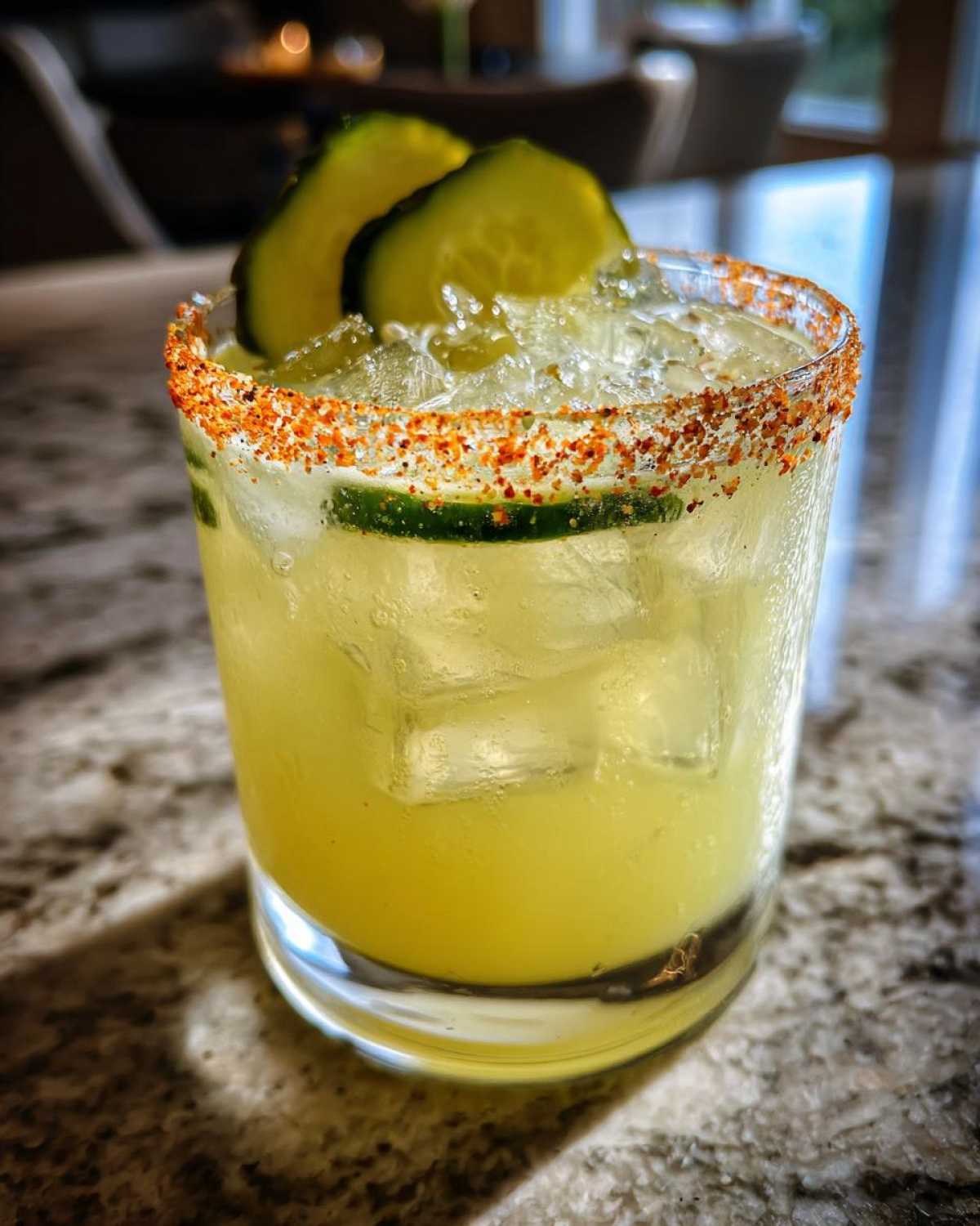 Close-up of a chilled Pickle Margarita in a rocks glass with a chili-lime rim and cucumber slices.