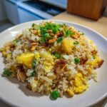 A close-up of a serving of amazing pineapple fried rice, featuring chunks of pineapple, scrambled egg, peas, and topped with cashews and green onions.