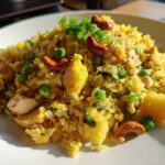 Close-up of a plate of vibrant yellow pineapple fried rice, featuring chunks of chicken, peas, pineapple, and topped with cashews and green onions.