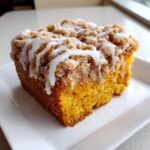 Close-up of a moist slice of pumpkin coffee cake topped with streusel and drizzled with white icing.