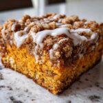 Close-up of a moist slice of pumpkin coffee cake topped with cinnamon streusel and white vanilla glaze.