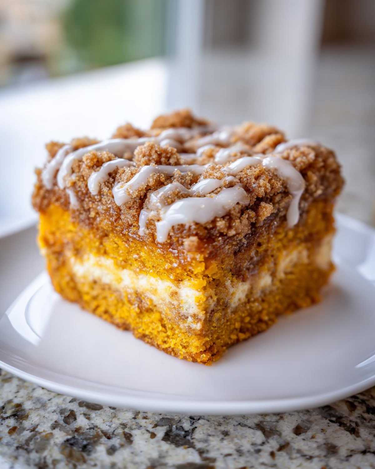 A close-up of a moist slice of pumpkin coffee cake featuring a cream cheese layer, streusel topping, and vanilla glaze.
