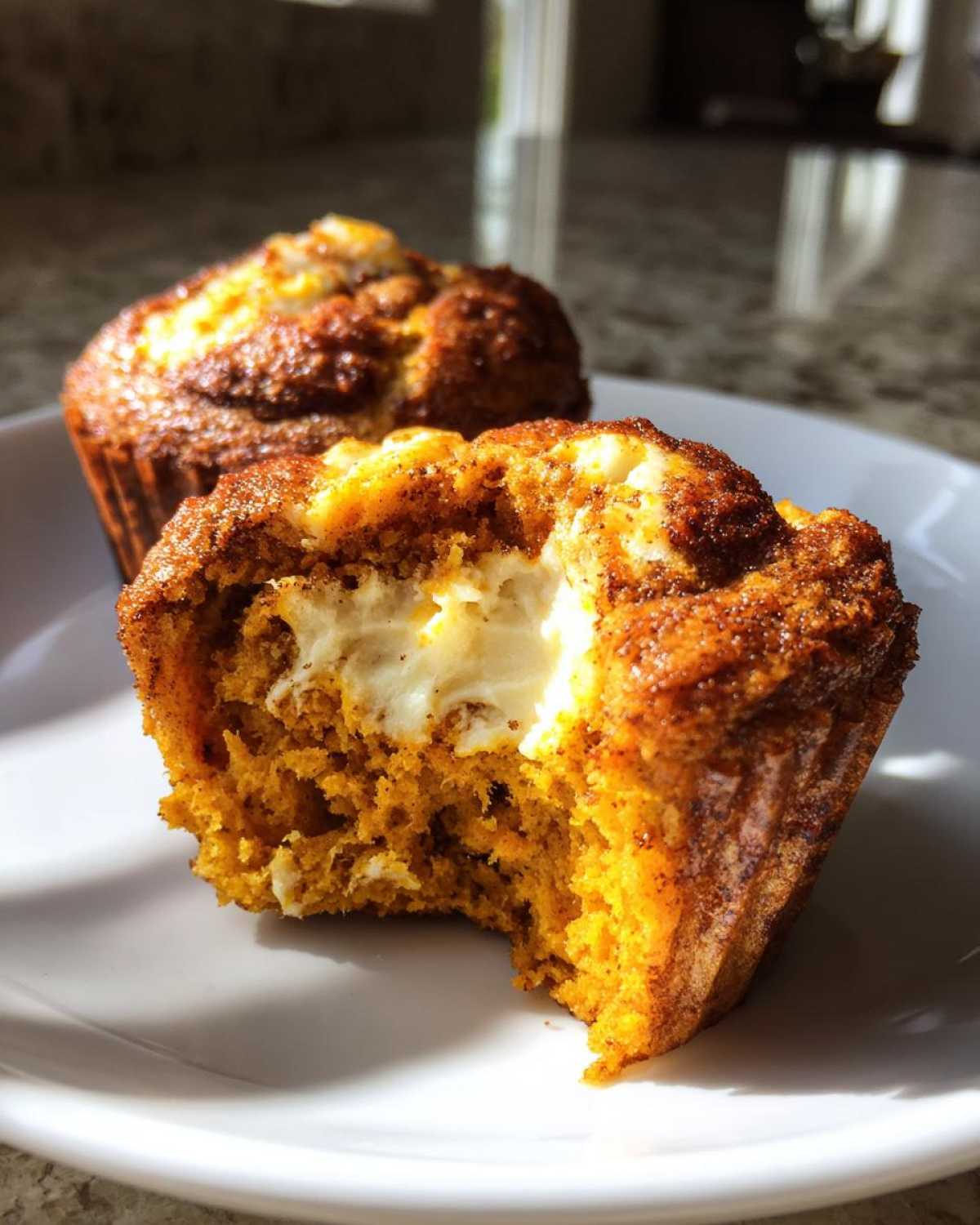 A close-up of a Pumpkin Cream Cheese Muffin with a bite taken out, revealing the creamy center.