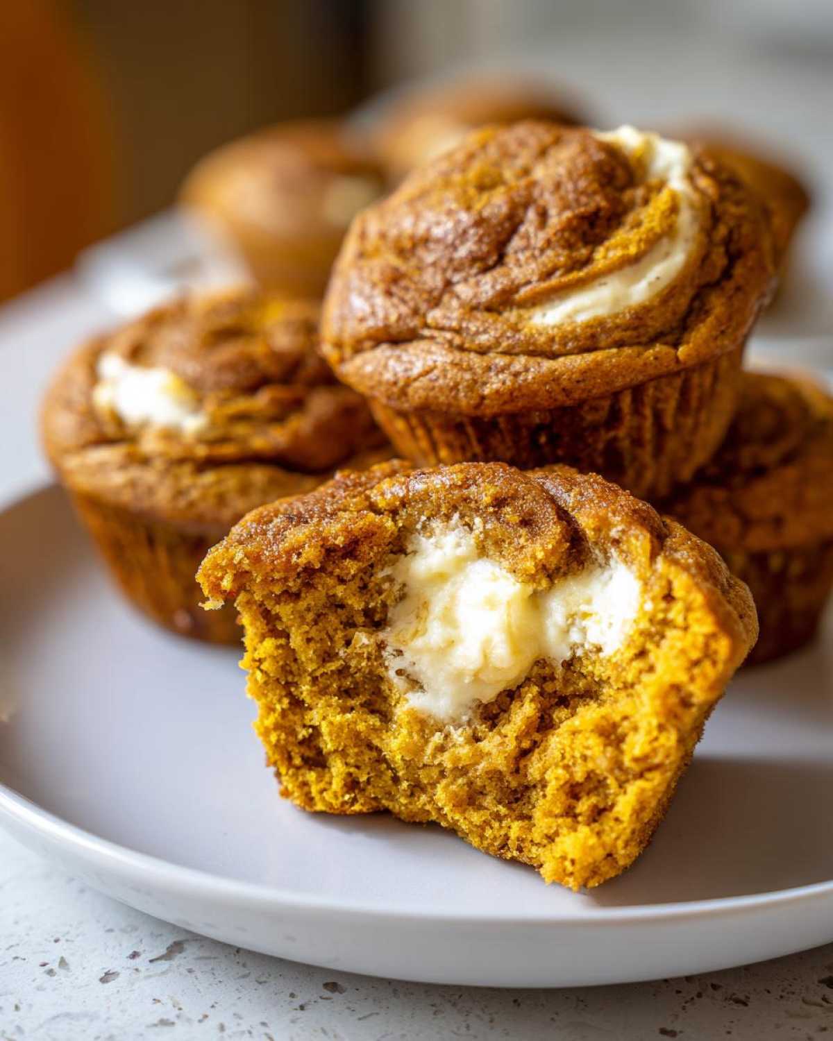 A close-up of a Pumpkin Cream Cheese Muffin broken open to show the creamy white filling inside.