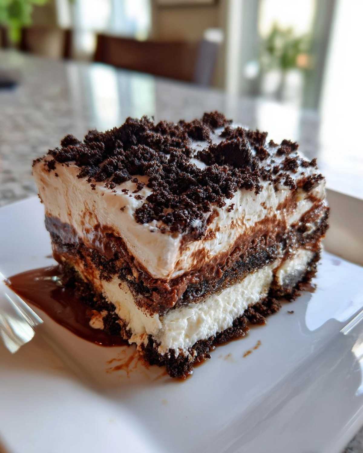 A rich slice of layered chocolate and cream decadent dessert topped with dark chocolate cookie crumbles.