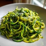 A close-up of vibrant Quick Zucchini Noodles with Pesto, topped with grated cheese, served on a white plate.