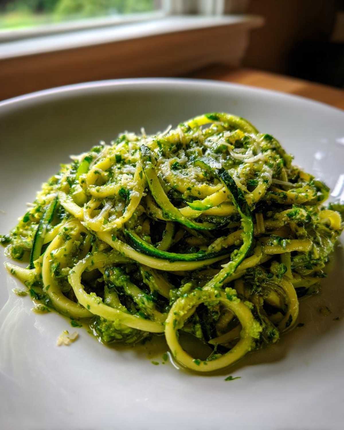 A close-up serving of Quick Zucchini Noodles with Pesto, topped with grated Parmesan cheese, on a white plate.