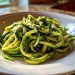 A close-up of Quick Zucchini Noodles with Pesto tossed in a white bowl, highlighting the green spirals.