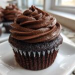 Close-up of a moist chocolate cupcake topped with a tall swirl of rich chocolate frosting, part of a batch of chocolate cupcakes.