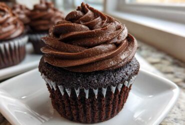 Close-up of a moist chocolate cupcake topped with a tall swirl of rich chocolate frosting, part of a batch of chocolate cupcakes.