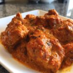 Close-up of tender chicken pieces smothered in a rich, orange-red sauce, characteristic of butter chicken.