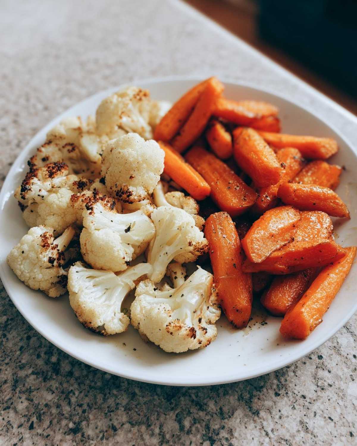 Close-up of perfectly seasoned roasted cauliflower and carrots served on a white plate.