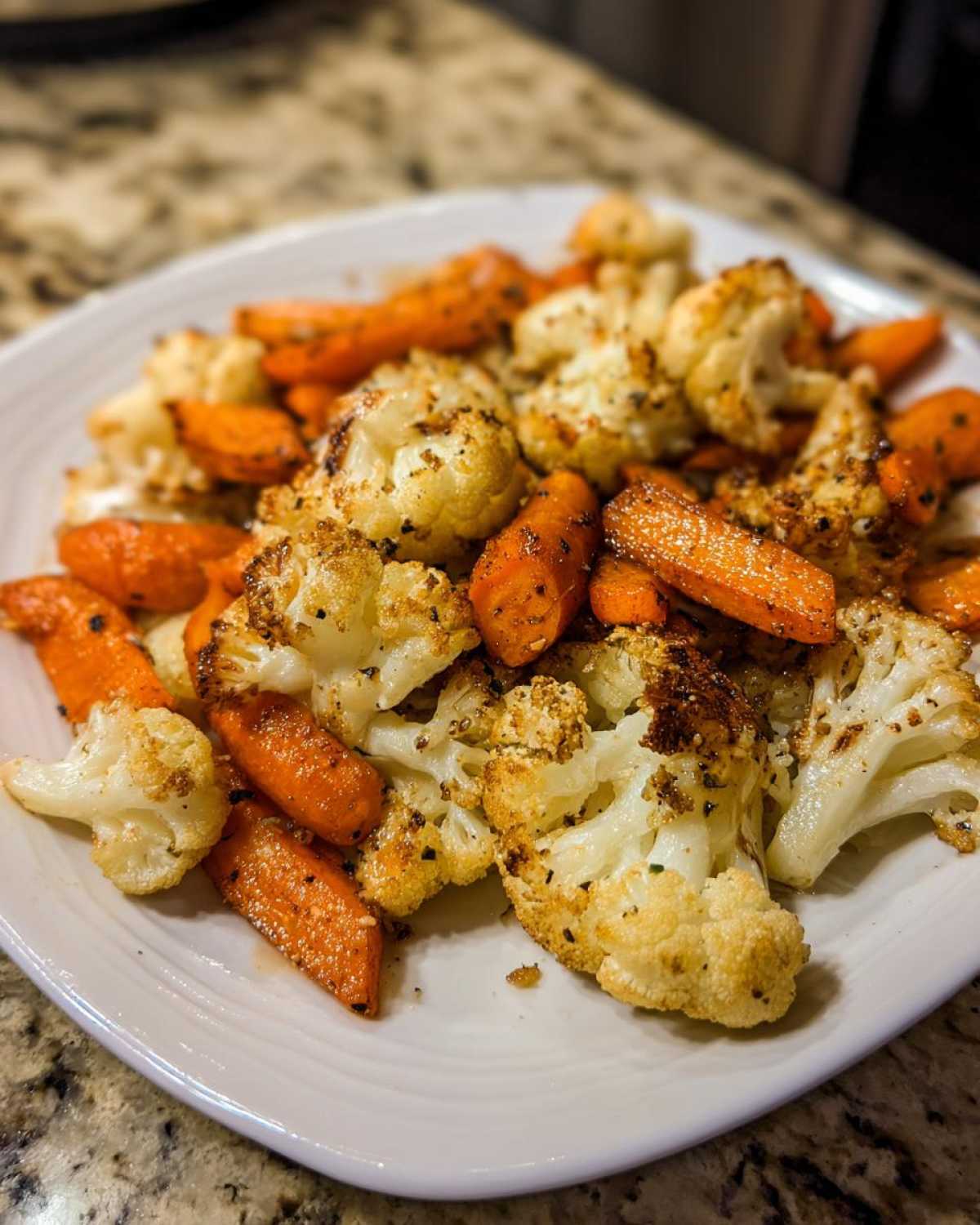 Close-up of perfectly seasoned roasted cauliflower and carrots served on a white plate.