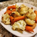 Close-up of perfectly roasted cauliflower and carrots seasoned with herbs on a white plate.