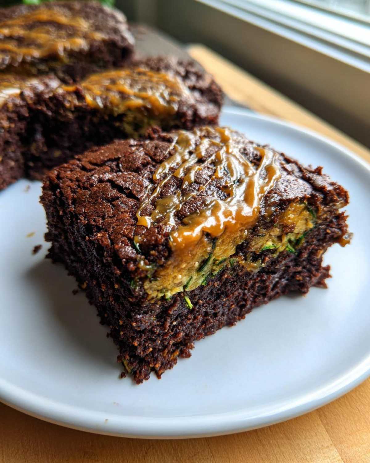 Close-up of a rich, fudgy Salted Caramel Swirl Zucchini Brownies square showing the green zucchini layer inside.