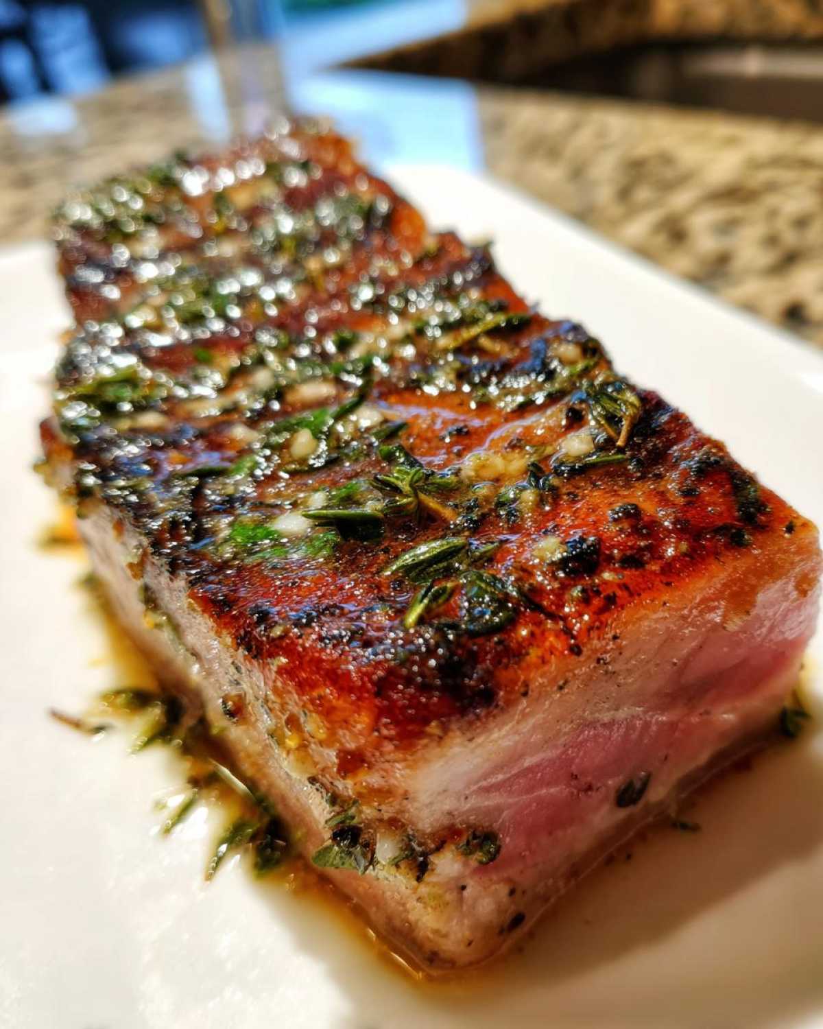 Close-up of a thick, seared tuna steak, cooked medium-rare and topped with a glistening herb and garlic glaze.