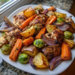 A close-up of Sheet Pan Harvest Chicken and Veggies featuring roasted chicken pieces, potatoes, carrots, Brussels sprouts, and red onion on a white plate.