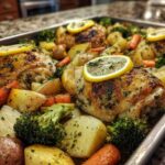 Close-up of roasted chicken thighs with crispy skin, potatoes, carrots, and broccoli on a sheet pan, garnished with lemon slices.