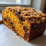 Close-up of a slice of simple pumpkin chocolate chip streusel bread showing the moist orange crumb and brown sugar topping.