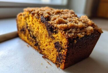 Close-up of a slice of simple pumpkin chocolate chip streusel bread showing the moist orange crumb and brown sugar topping.