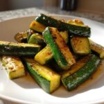 A close-up of glistening Simple Roasted Zucchini Spears seasoned with spices, piled on a white plate.
