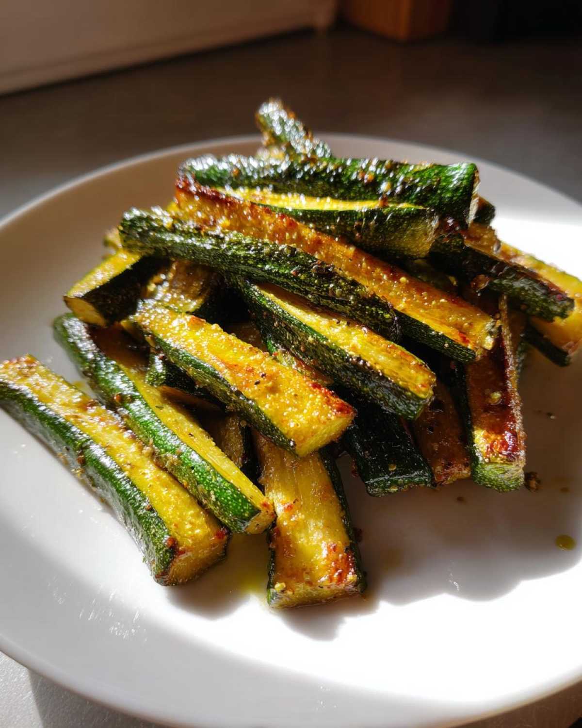 A pile of seasoned Simple Roasted Zucchini Spears served on a white plate, glistening under natural light.