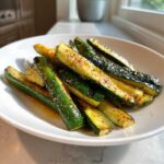 A white bowl filled with perfectly cooked Simple Roasted Zucchini Spears, seasoned with pepper.