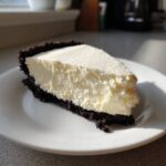 A perfect slice of creamy No bake cheesecake featuring a thick white filling and a dark chocolate cookie crust, served on a white plate.