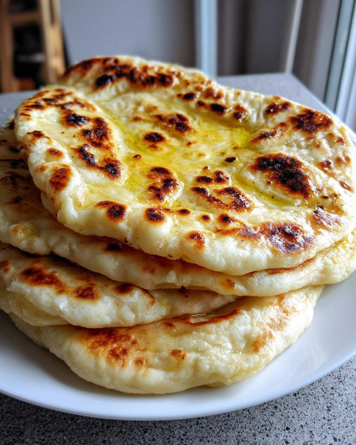 A stack of freshly made, soft naan bread brushed with melted butter, showing golden-brown charred spots.
