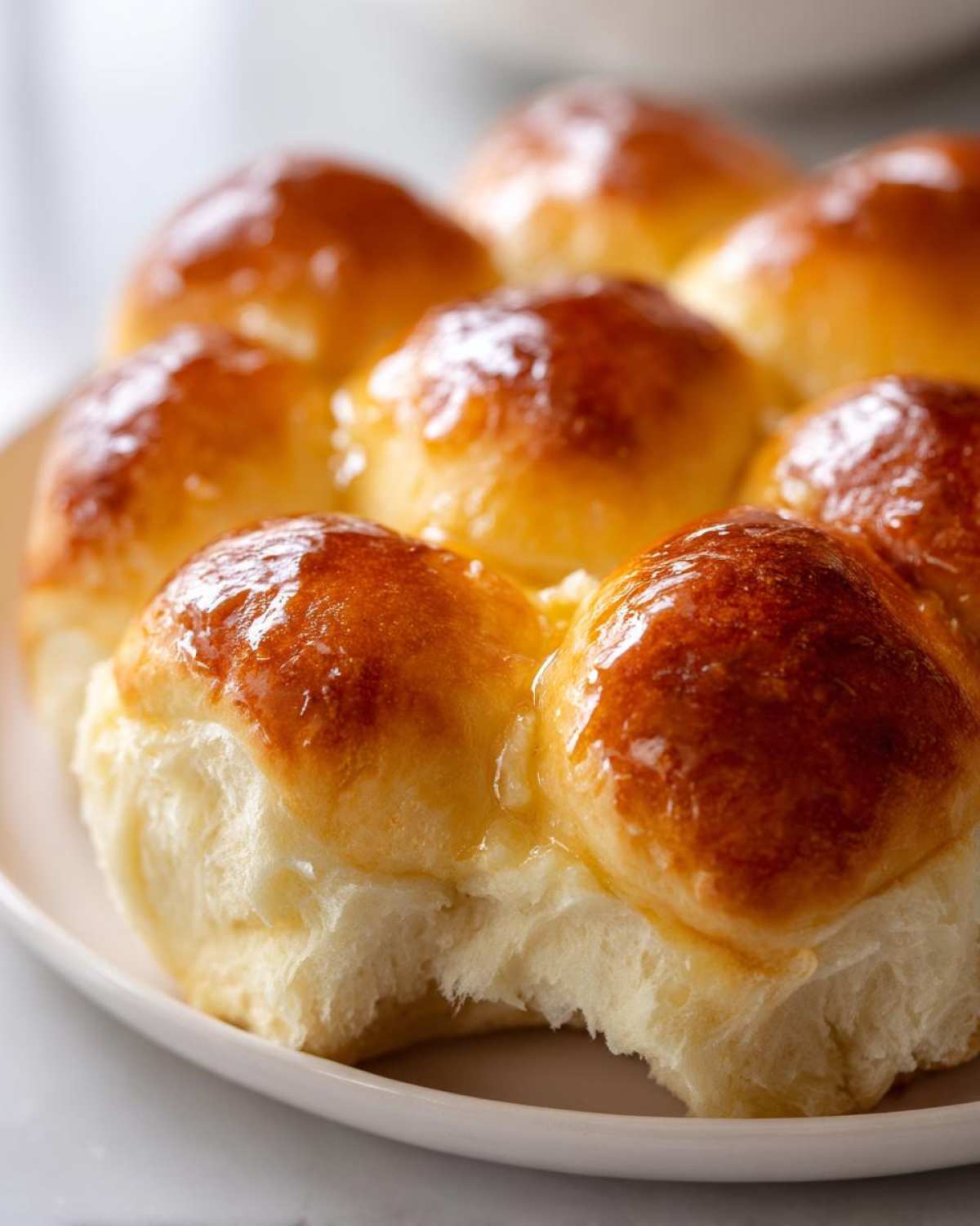 Close-up of freshly baked, soft buttery rolls with a shiny golden-brown top, one roll has a bite taken out.