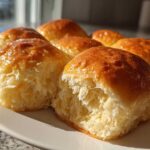 A cluster of freshly baked, soft buttery rolls with a shiny golden-brown top, showing the fluffy interior.