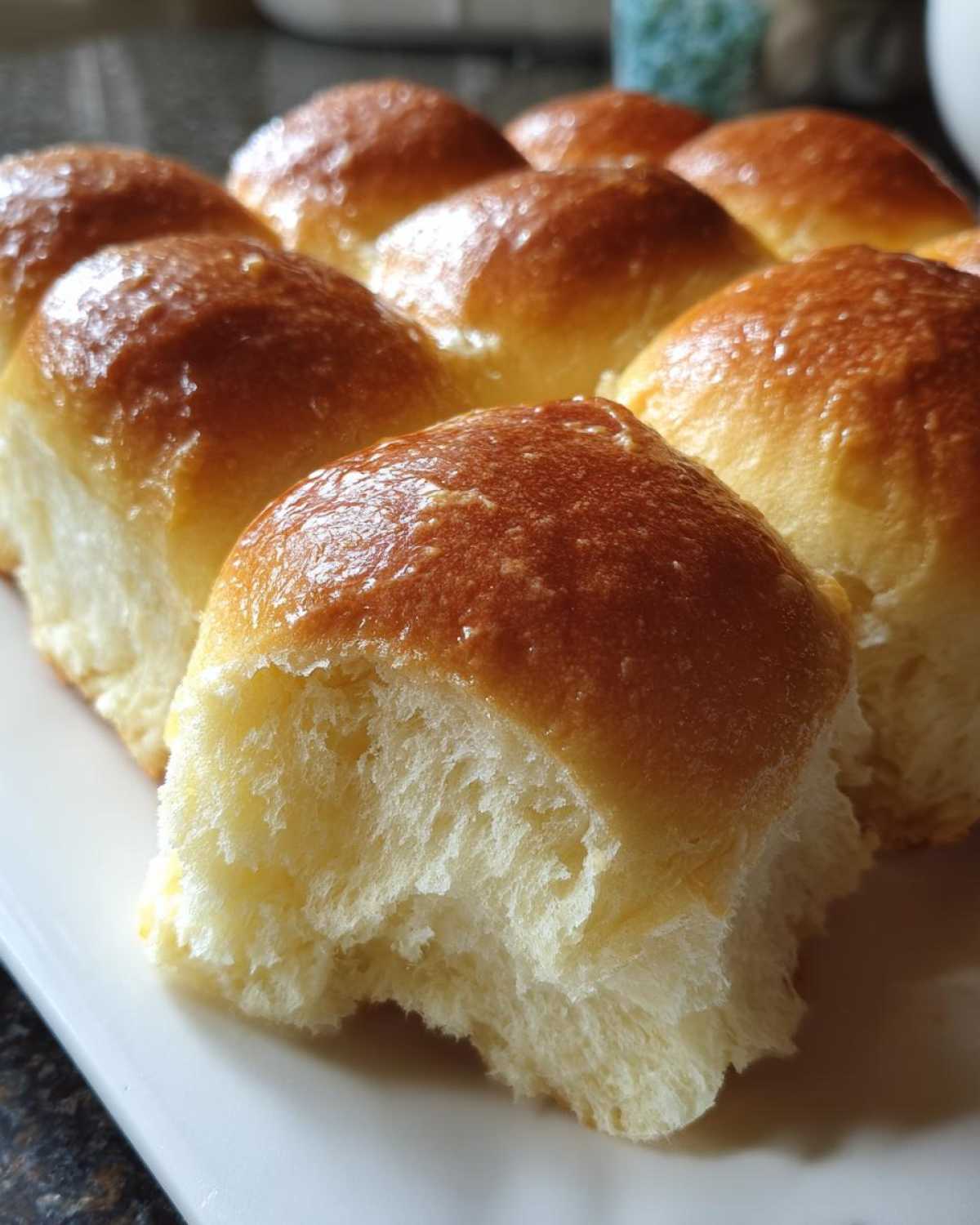 Close-up of soft, fluffy dinner rolls fresh from the oven, showing a pull-apart texture and buttery glaze. These are the 1-Hour Soft Buttery Rolls.
