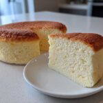 A slice of incredibly soft and fluffy Japanese cotton cheesecake resting on a white plate next to the remaining whole cake.