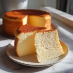 Two slices of soft and fluffy Japanese cotton cheesecake showing the airy interior texture, with the rest of the cake in the background.