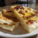 Close-up of soft, fluffy naan bread stacked on a white plate, brushed with melted butter and herbs.