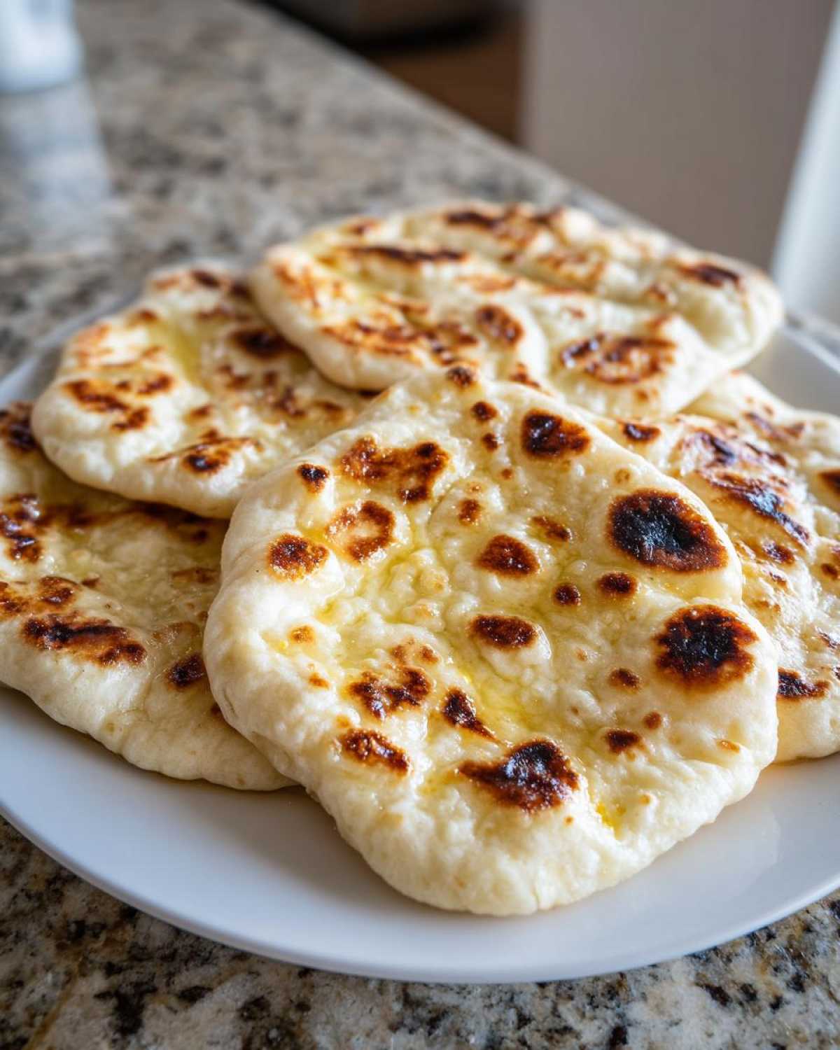 A stack of freshly cooked, soft naan bread pieces brushed with butter, showing characteristic charred spots.