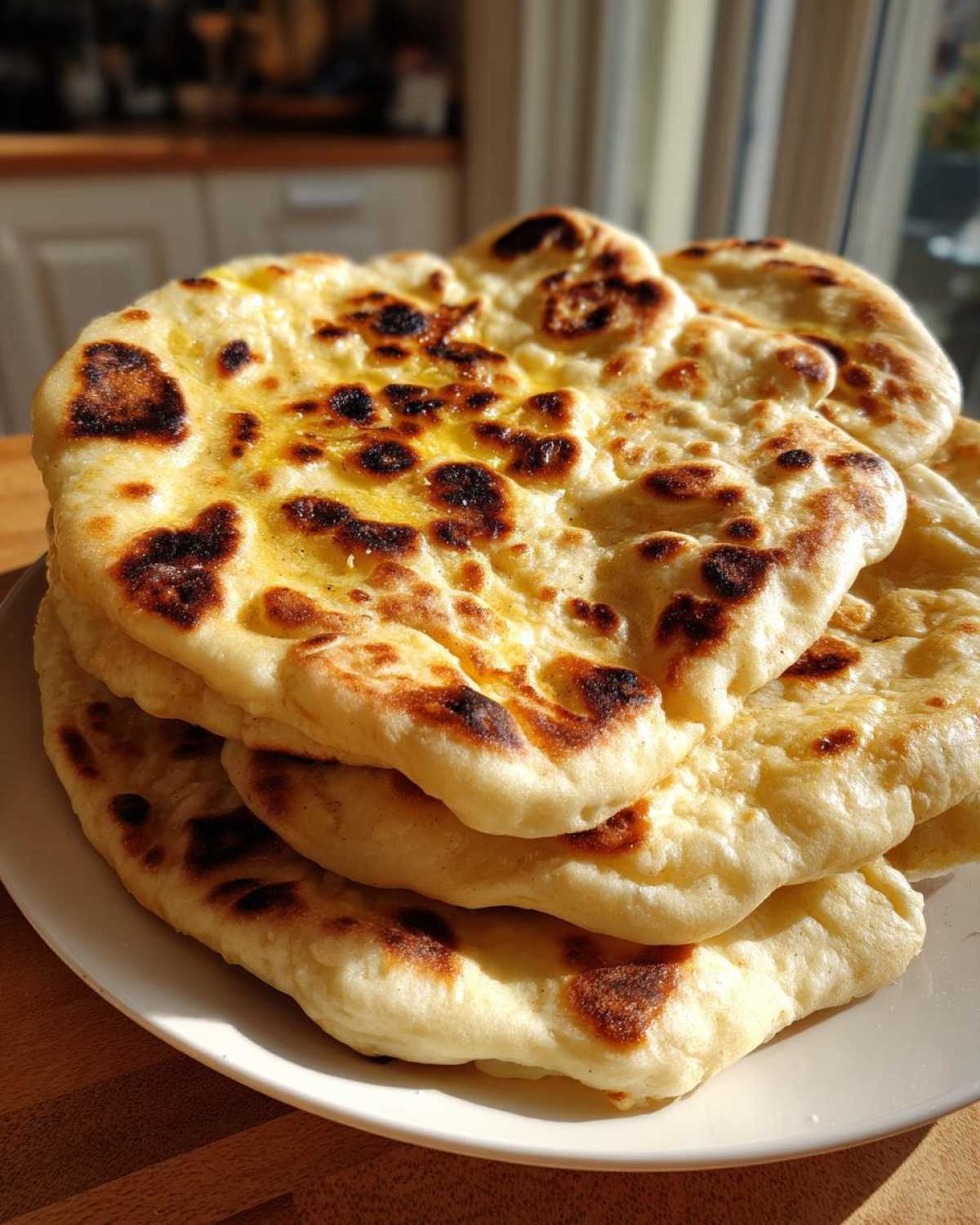 A stack of freshly made, soft naan bread brushed with butter, showing characteristic charred bubbles.