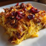 A square serving of baked spaghetti squash casserole topped with dried cranberries and pecans.