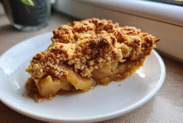 A close-up of a warm slice of Spiced Pear Crumble on a white plate, showing soft spiced pears and a thick, crunchy topping.