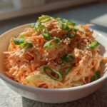 Close-up of a vibrant spicy kani salad served in a white bowl, topped with green onions and sesame seeds.