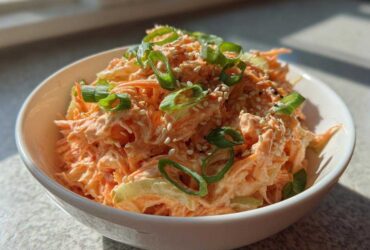 Close-up of a vibrant spicy kani salad served in a white bowl, topped with green onions and sesame seeds.