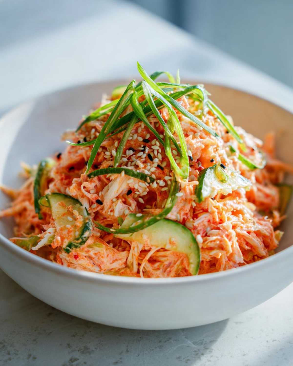 Close-up of a vibrant Spicy Kani Salad featuring shredded crab mix, cucumber slices, topped with sesame seeds and green onions.