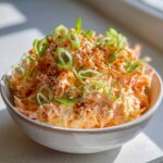 Close-up of a creamy, spicy kani salad topped with sliced green onions and sesame seeds in a light bowl.