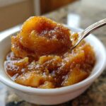 A spoonful of rich, spiced apple pie filling being lifted from a small white bowl.