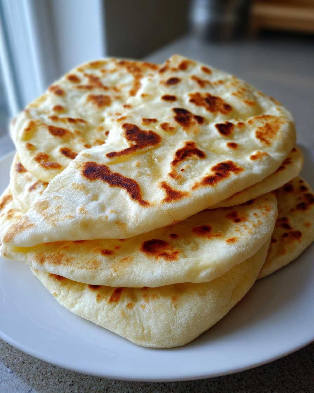 A close-up stack of freshly cooked, puffy pita bread rounds with golden-brown charred spots.