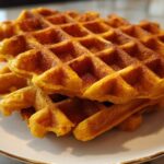 A close-up stack of golden brown, perfectly textured pumpkin waffles on a white plate.