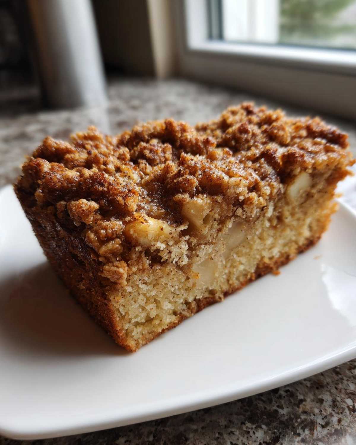 A close-up slice of moist super easy apple crisp coffee cake featuring visible apple chunks and a thick cinnamon streusel topping.