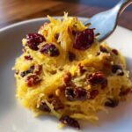 A fork lifts a bite of sweet spaghetti squash mixed with dried cranberries, perfect for thanksgiving recipes.