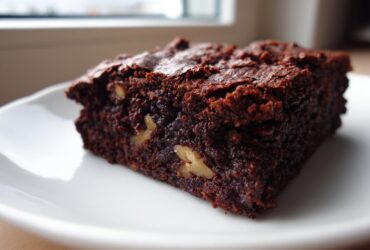 A rich, dark chocolate square of tasty healthy date brownies featuring visible pieces of walnuts on a white plate.