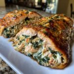 Close-up of a golden-brown stuffed salmon fillet, sliced to show the creamy spinach and salmon filling inside.